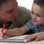 Father and son lying on floor practising writing together
