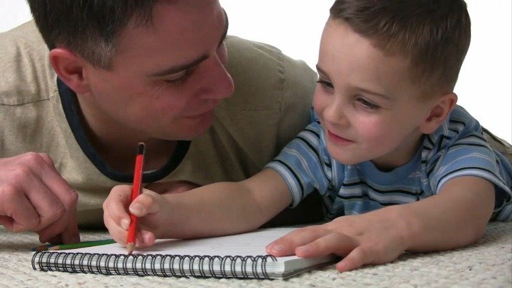 Father and son lying on floor practising writing together